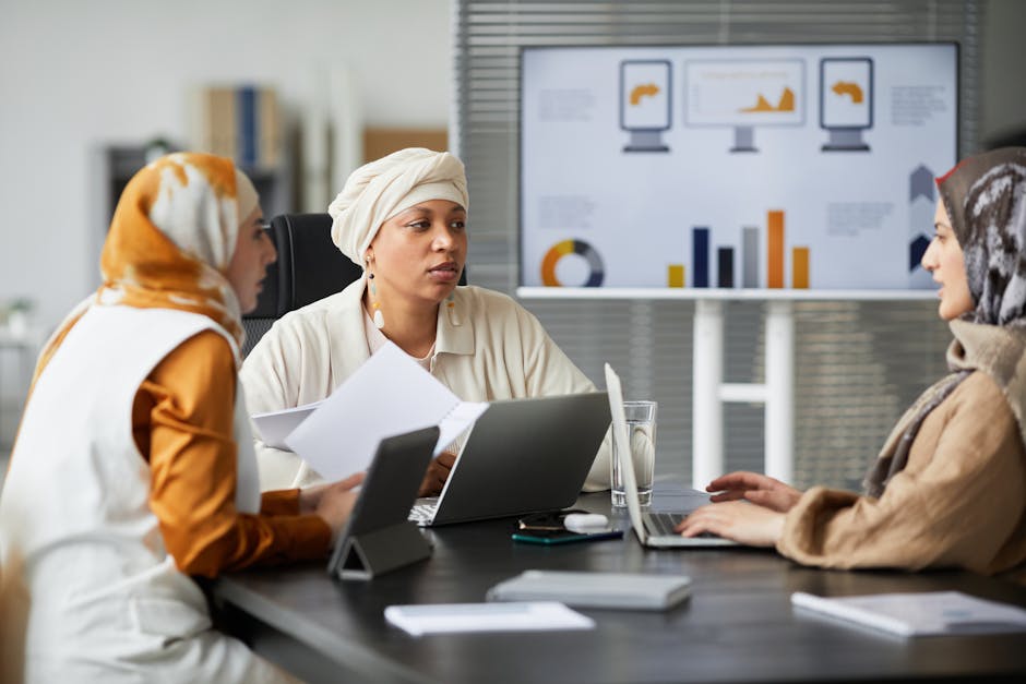 Three diverse women in headscarves engaged in a business meeting at a modern office with charts.